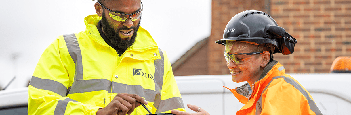 Two Kier employees in workgear discussing the contents of a document while smiling