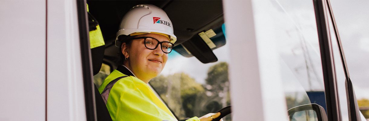 Image of a Kier employee in the front seat of a HGV wearing a helmet and a high vis jacket